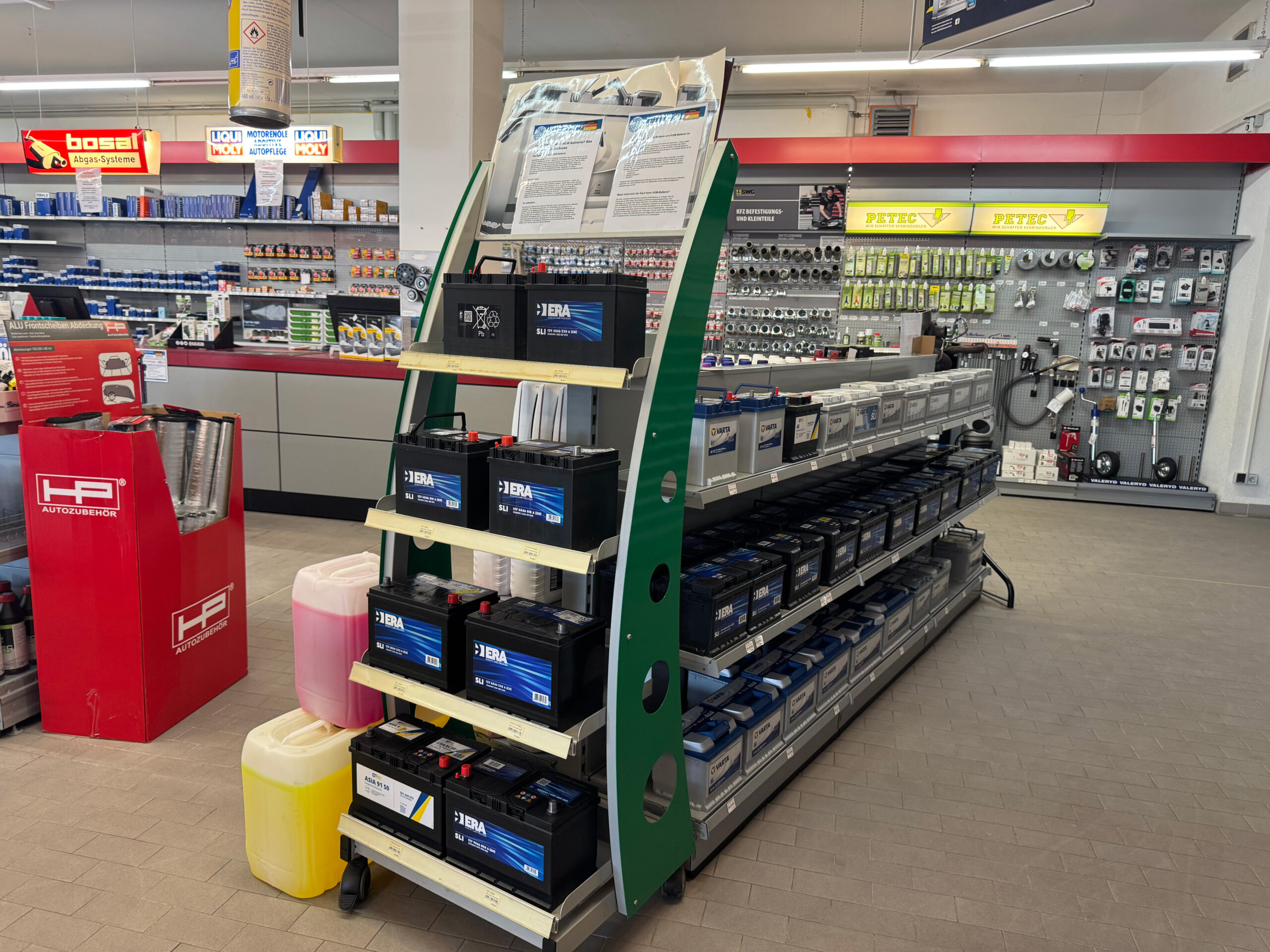 Verkaufsregal mit Autobatterien, Kanistern mit Flüssigkeiten und Zubehörteilen, dahinter Regale mit Kleinteilen.