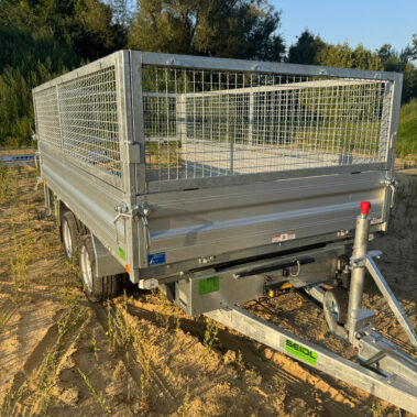 Vorderansicht eines geschlossenen Kippanhängers mit Gitteraufsätzen, abgestützt mit Deichselstütze, im Sonnenlicht.