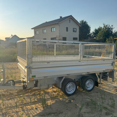 Schrägansicht eines geschlossenen Kippanhängers mit Gitteraufsatz, geparkt auf einer unbefestigten Fläche.