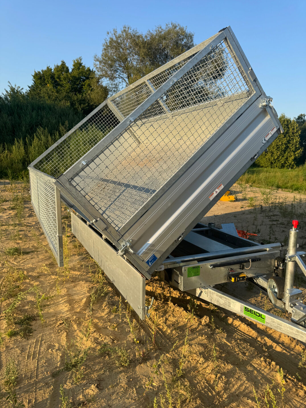 Kippanhänger mit geöffnetem Aufbau, Ladefläche nach hinten gekippt, um Material abzuladen.