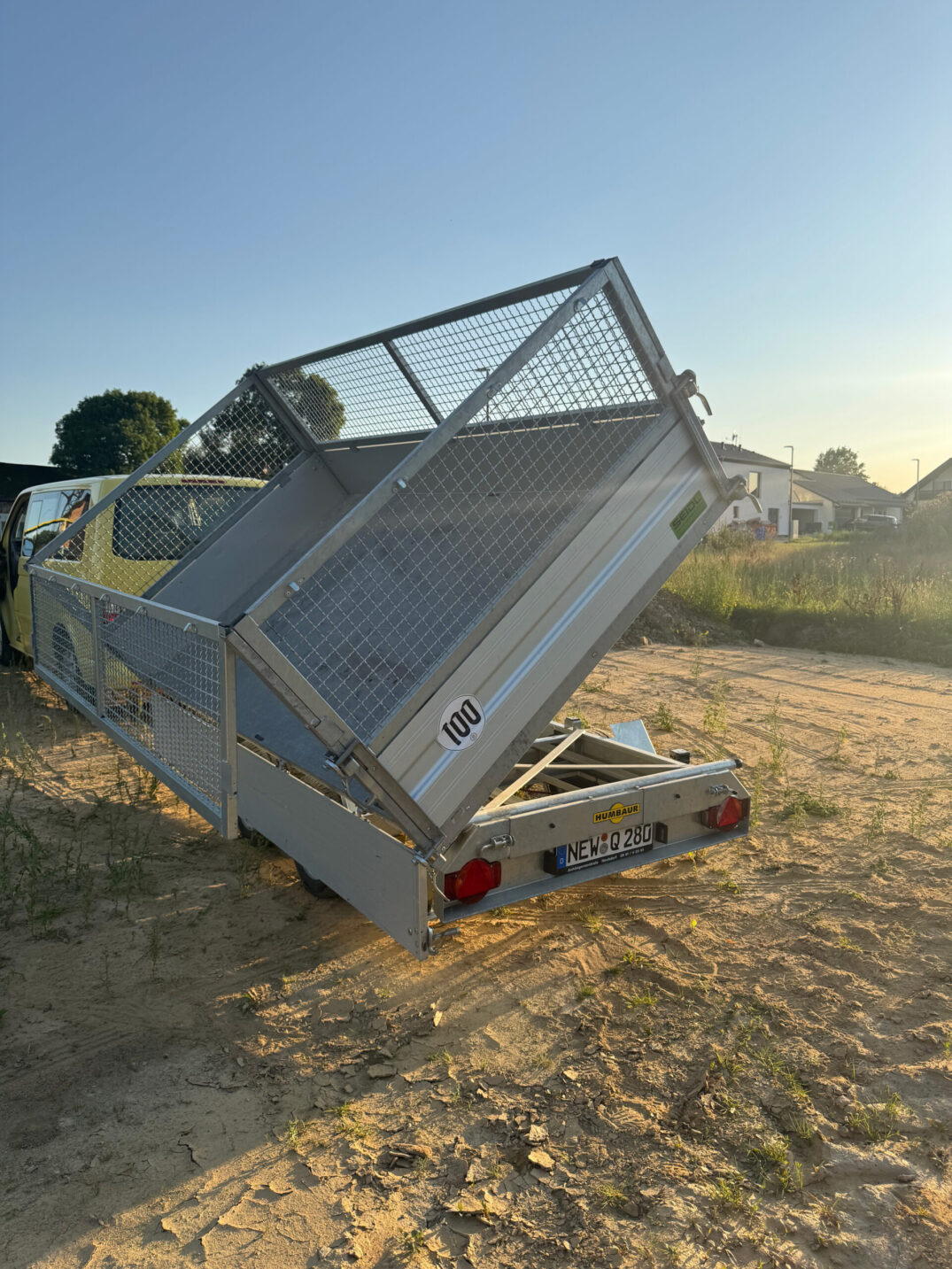 Schrägheckansicht des angekippten Kippanhängers, im Hintergrund ein gelbes Fahrzeug.