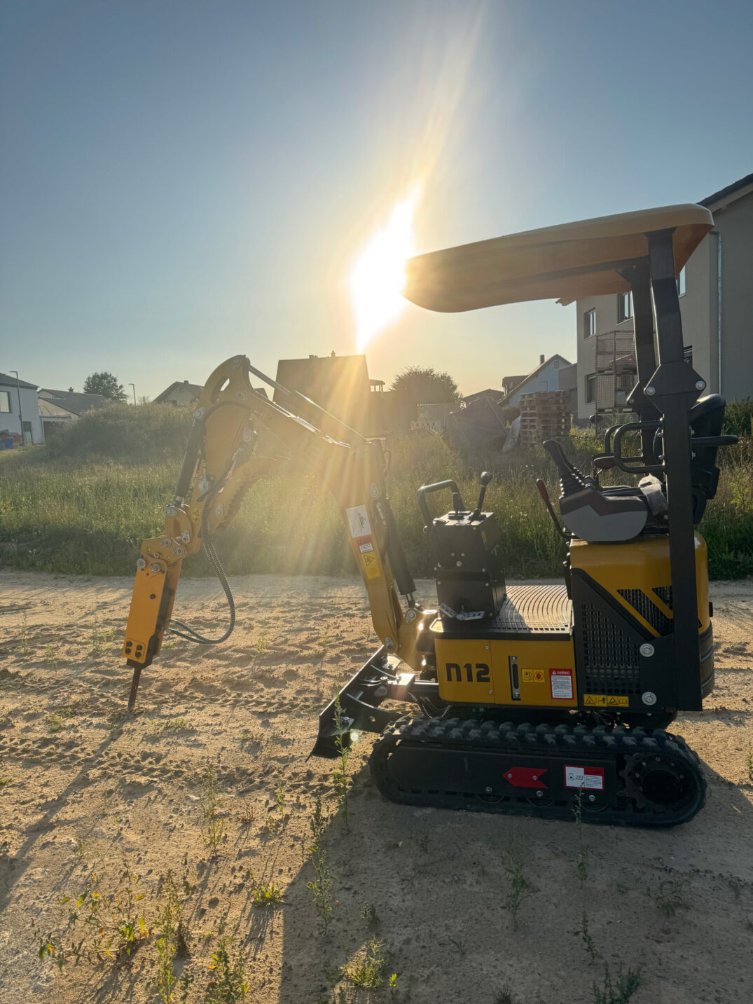 Gelber Kettenbagger mit Hydraulikhammer-Aufsatz, im Profil vor tiefstehender Sonne.