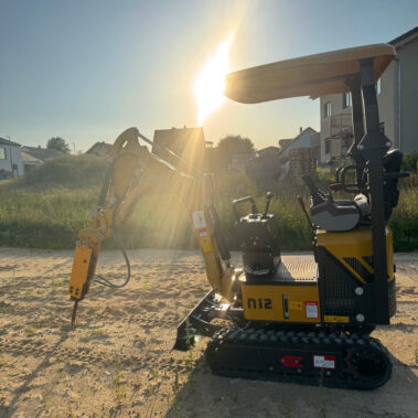 Gelber Kettenbagger mit Hydraulikhammer-Aufsatz, im Profil vor tiefstehender Sonne.