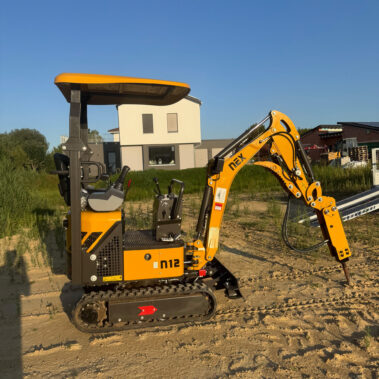 Gelber Minibagger mit Hydraulikhammer-Aufsatz, geparkt auf sandigem Untergrund.