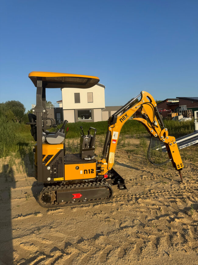 Minibagger-4 Gelber Minibagger mit Hydraulikhammer-Aufsatz, geparkt auf sandigem Untergrund.