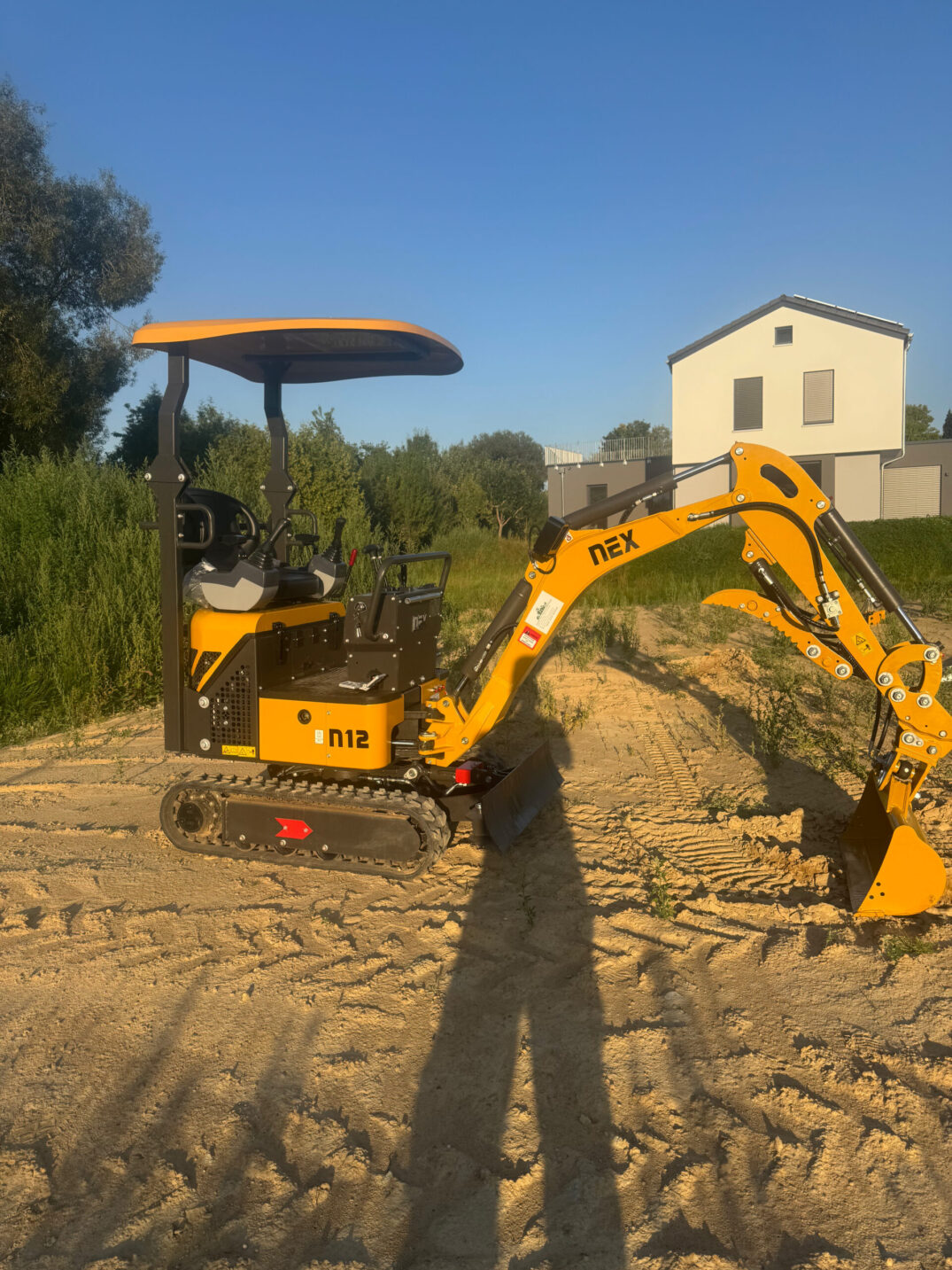 Gelber Minibagger mit montierter Ladeschaufel, Seitenansicht bei Abendlicht.
