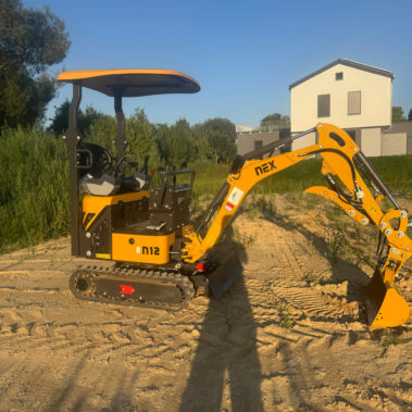 Gelber Minibagger mit montierter Ladeschaufel, Seitenansicht bei Abendlicht.
