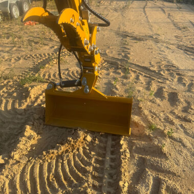 Nahaufnahme einer gelben Ladeschaufel mit groben Zähnen auf sandigem Boden, daneben Kettenabdrücke.