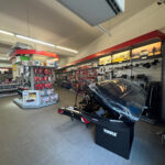 Verkaufsfläche mit Regalen voller Autozubehör und einem Thule-Fahrradträger mit Dachbox im Vordergrund.