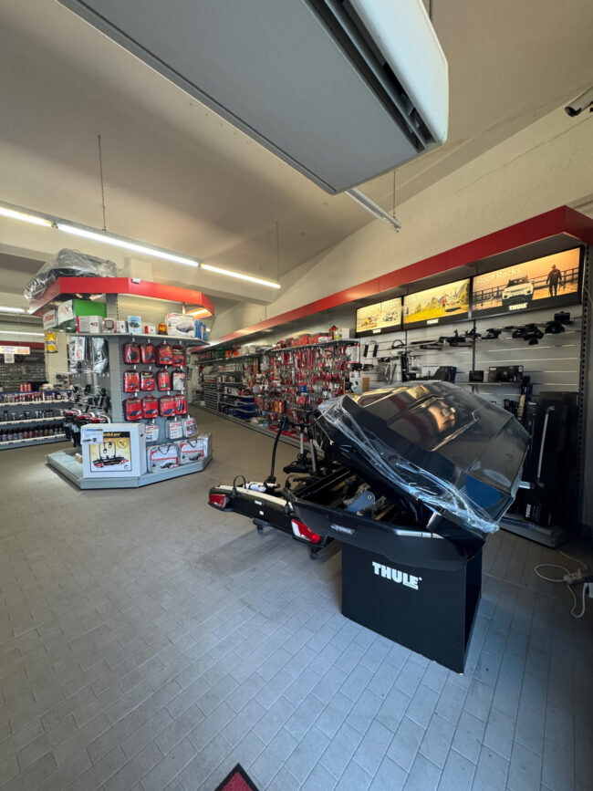 Nicks Automobile-1 Verkaufsfläche mit Regalen voller Autozubehör und einem Thule-Fahrradträger mit Dachbox im Vordergrund.