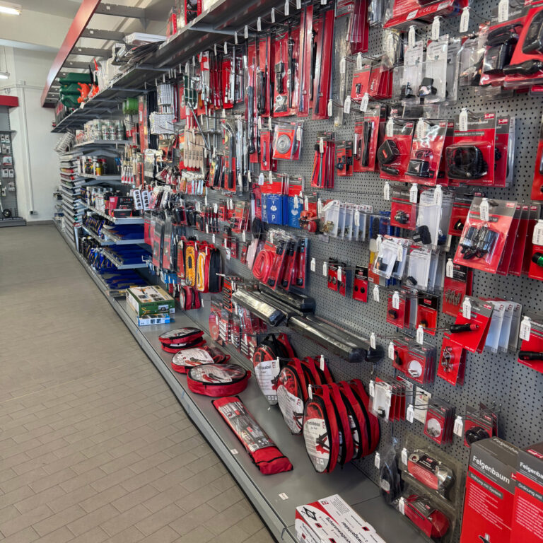 Hakenwand mit verschiedenen Kfz-Ersatzteilen, Werkzeugen und Zubehör in roten Verpackungen.