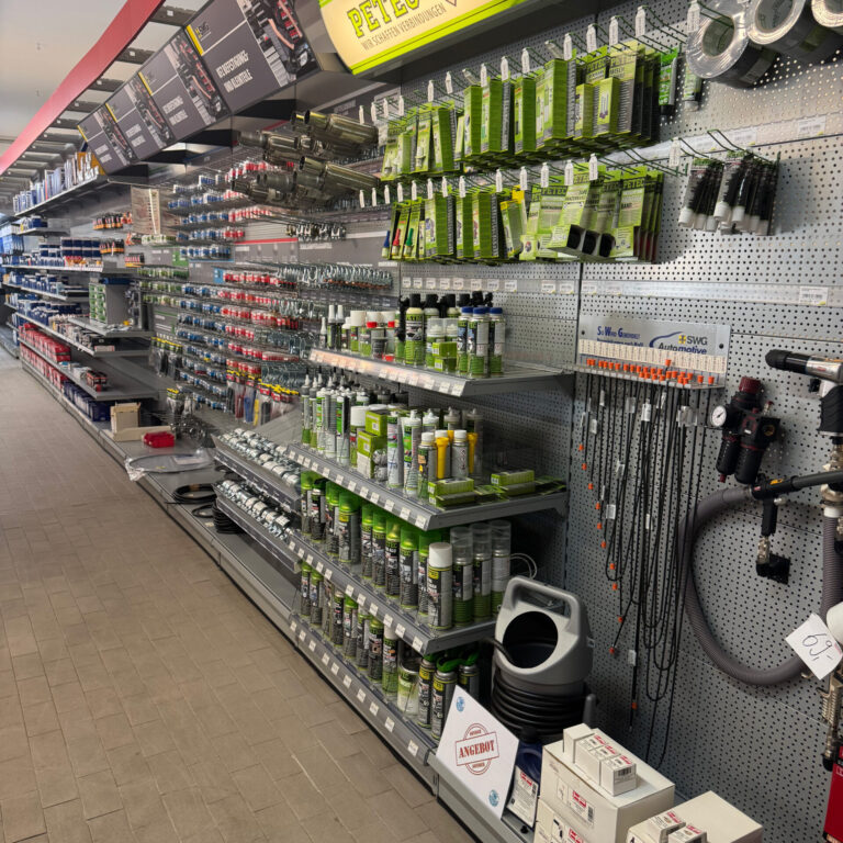 Regalwand mit PETEC-Produkten, unter anderem Dicht- und Klebemittel in grüner Verpackung, sowie weiteren Autozubehörartikeln.