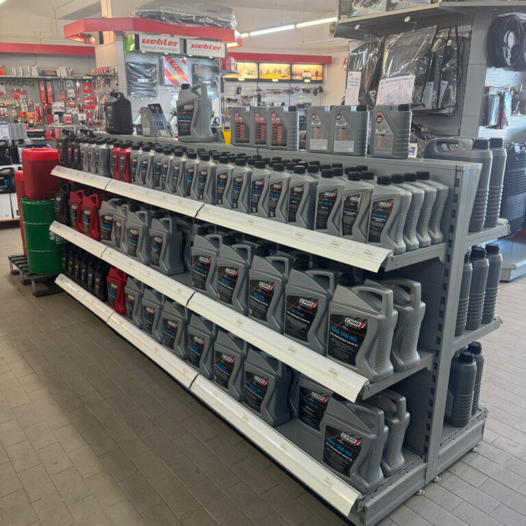 Verkaufsregal mit mehreren Reihen Motoröl in grauen Kunststoffkanistern, vorne und auf den oberen Regalböden.