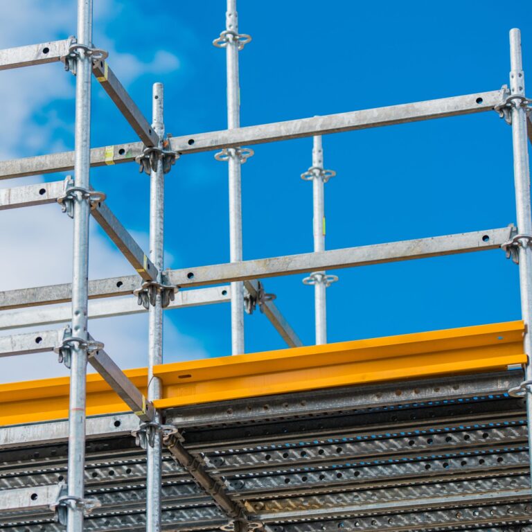Alternativtext: Metallgerüst mit gelbem Seitenschutz vor blauem Himmel auf einer Baustelle.