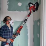 Person schleift Wand mit elektrischem Trockenbauschleifer