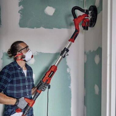 Person schleift Wand mit elektrischem Trockenbauschleifer