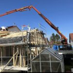 Kran montiert Holzelemente auf ein Haus im Bau, Arbeiter stehen auf dem Dachgerüst.