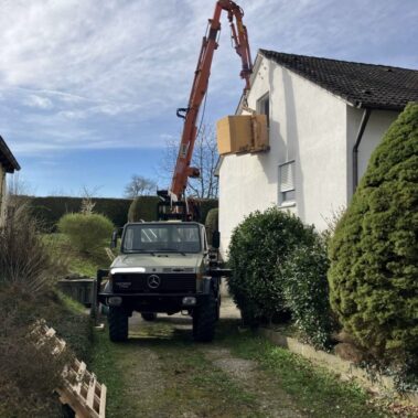 Kran hebt große Kiste an die Außenwand eines Hauses, Lieferung durch Fensterhöhe.