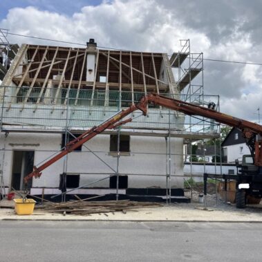Sanierung eines Hauses mit offenem Dachstuhl, Kran unterstützt Bauarbeiten am Gerüst.